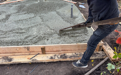 A man is laying concrete on a wooden platform