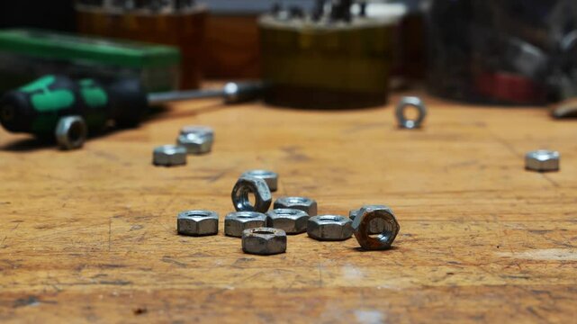 Close up Used metal nuts are lying on a wooden workbench, and another screw is rolling out from the side. Nuts are used in industry and in the home.