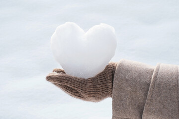 Female hand in brown glove holding heart shaped snowball on white background.