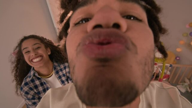 POV shot of Biracial young couple and newly minted parents playing with their baby in cozy nursery, father tossing t in air, then catching and kissing with all love and tenderness