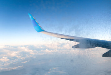 The wing of a plane is seen in the sky with clouds in the background