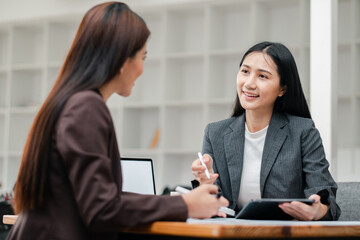 Two businesswomen engaged in a meeting, discussing work with digital tablets and documents in a modern office environment.