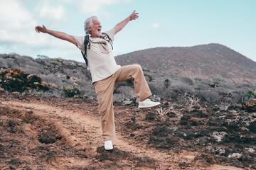 Crazy excited grandparent jumping in outdoors excursion raising one leg with open arms. Senior bearded man enjoying life and retirement