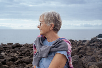 Portrait of smiling mature woman sitting outdoors along seaside enjoying freedom and healthy lifestyle, elderly carefree pensioner admiring landscape of atlantic ocean in Tenerife, Canary Islands
