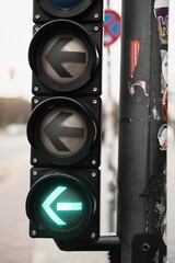 Detailed view of a traffic light showing a green left-turn arrow, mounted on a pole with urban...