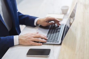 Against a softly blurred office scene, a man's hands are shown in detail, typing on a...