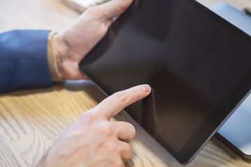 Closeup of a man's finger making contact with a state-of-the-art tablet screen on a desk, amidst the indistinct buzz of a light office environment