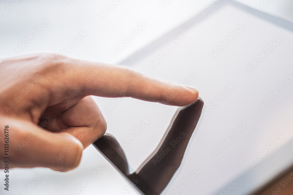 Poster man's finger touching a digital tablet screen placed on a desk, surrounded by the vague surroundings