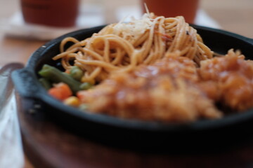 A delicious combination of crispy chicken and flavorful noodles served on a sizzling plate with vegetables