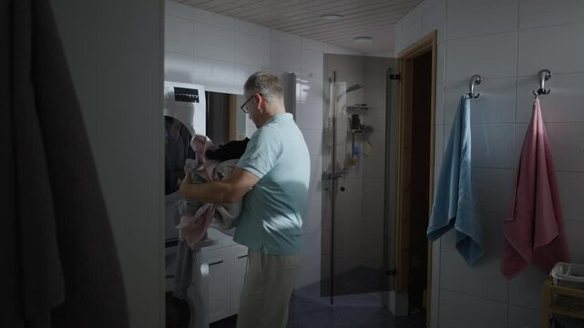 Middle-aged man loading clothes into the washing machine or dryer. Laundry cleaning. Housework, homework, male housekeeper. Husband man doing laundry at home. Washer and dryer at home.
