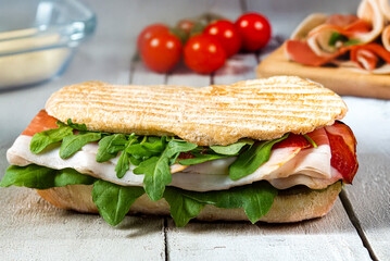 Delicious sandwich with  ham and arugula on rustic wooden table, close-up