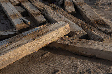 Weathered wooden beams rest on sandy beach. Nature and texture highlighted. Sunset adds warmth.