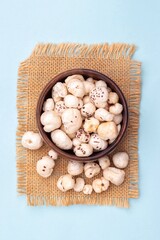 Top View of Makhana or Fox Nut in a Wooden Bowl on Burlap Fabric Isolated on Light Blue Background with Copy Space, Also Known as LEuryale Ferox, otus Seed Pop or Gorgon Nut