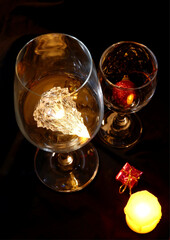 Christmas ornament and light in wine glasses with a candle at night on a black background. Table setting for drinking in darkness with concept of romantic, party, dinner, holiday, and Xmas festival.