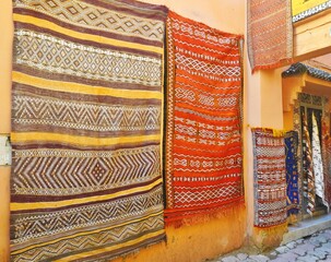 Colorful antique rugs with intricate patterns hanging on a wall in an outdoor market in Morocco