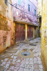 Curved stone paved street open to the sky above with ancient crumbling faded painted walls