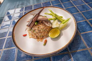 Fried rice with mackerel and include chili, lime and cucumber in plate on blue tiled surface