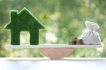 Model house and money bag on wood scale seesaw on natural green background, Business investment and real estate concept