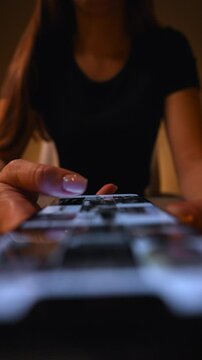 Vertical shot from above of woman watching and reading online news on smartphone, scrolling up and down looking in phone screen, browsing social media in dark room. Shooting in slow motion.