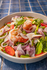 Close up, Spicy seafood salad in bowl on blue tiled surface, Thai dish