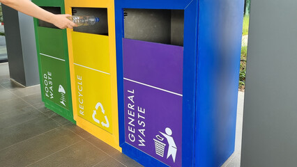 woman hand puts plastic bottle into a trash can by separating trash for different types of waste by icon and color of bin and recycling waste. recycling and sustainability concept
