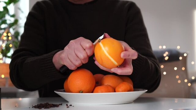 Pomander oranges being carved with a zester by woman in sweater at table. Bokeh.