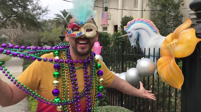 A young latin tourist male, wearing mask, costumes and necklaces celebrating Mardi Gras through the streets while taking a selfie with his cellphone in New Orleans