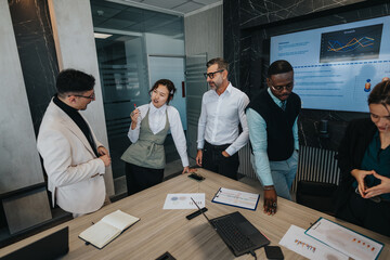 Diverse group of people engaged in a collaborative business meeting, discussing charts and data in a modern office. Teamwork and communication are highlighted as key elements in this corporate