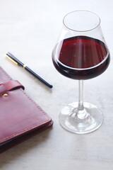 赤ワインを飲みながら、ワインレッドの革のシステム手帳に日記をつけているイメージ
