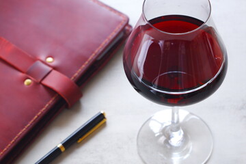 赤ワインを飲みながら、ワインレッドの革のシステム手帳に日記をつけているイメージ
