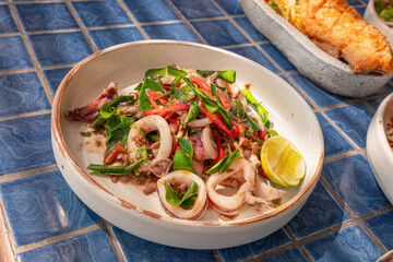 Spicy fried squid with shrimp paste in plate on blue tiled surface, Thai dish