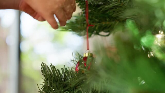 Young caucasian boy hangs a Christmas bauble decoration on tree