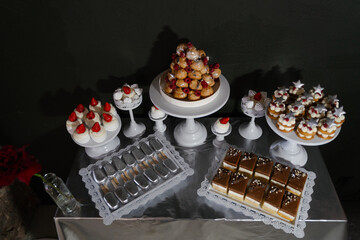 Candy bar with confectionery desserts on silver tablecloth on dark background, top view