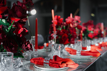 Festive table decorated with red roses, candles, napkins and served with silver tablecloth and dishes in a gray room