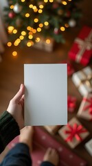 Obraz premium Woman holding blank card against background of Christmas gifts, holiday lights and festive decor.