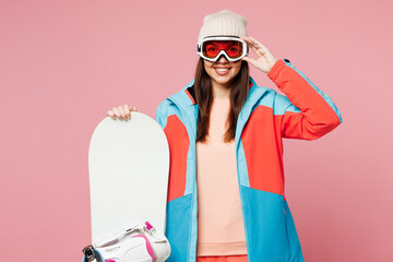 Snowboarder young happy woman wear warm blue padded jacket ski goggles mask spend extreme weekend winter season in mountains hold snowboard look camera isolated on plain pink background Hobby concept