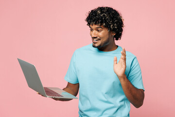 Young IT Indian man he wears blue t-shirt casual clothes hold use work on laptop pc computer waving...