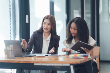 Collaborative Strategy:  Two diverse businesswomen, colleagues, or partners engage in a productive discussion over a laptop and tablet, demonstrating teamwork, communication, and problem-solving.  