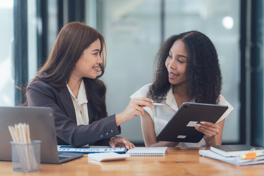 Collaborative Businesswomen: Two diverse businesswomen engaged in a productive discussion, reviewing data on a tablet, showcasing the power of collaboration and teamwork in the modern workplace.