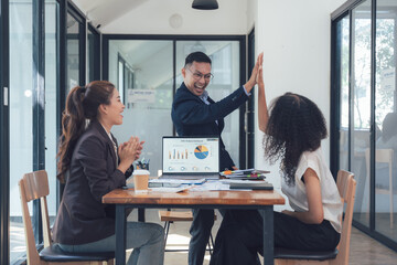 Obraz premium High-Five Success: A diverse team celebrates a business achievement with a celebratory high-five. The image shows three professionals in a modern office setting, reviewing data on a laptop. 