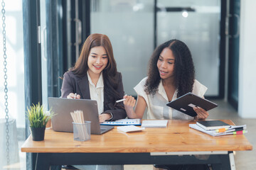 Collaborative Businesswomen: Two diverse businesswomen working together on a project using laptop and tablet in modern office.  
