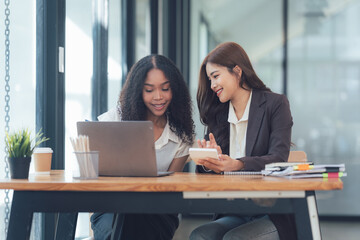 Collaborative Success: Two young businesswomen review data on a tablet and laptop, showcasing teamwork and modern office collaboration.  