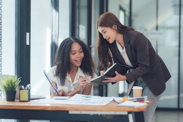 Collaborative Success: Two diverse businesswomen engage in a productive meeting, reviewing documents and brainstorming ideas together in a modern office setting.  