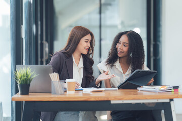 Collaborative Success: Two diverse businesswomen engage in a productive discussion, their smiles and focused expressions conveying a shared vision and collaborative spirit.