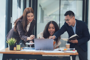 Team Collaboration: Three diverse professionals huddle around a laptop, sharing ideas and...