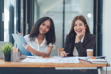 Confident Businesswomen Collaboration: Two smiling businesswomen working together at a desk, showcasing their confidence and successful partnership.