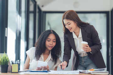 Collaborative Spirit: Two diverse businesswomen, one with a coffee cup in hand, engage in a...