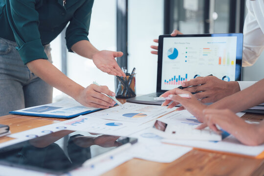 Teamwork Makes the Dream Work: A close-up shot of a team collaborating around a table, deeply engrossed in analyzing financial charts and graphs on laptops and tablets.