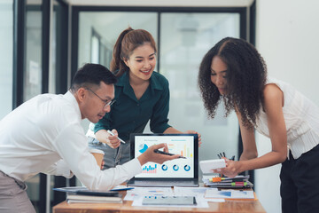 Collaborative Analysis: A diverse team of business professionals collaborates around a laptop, deeply engaged in analyzing data charts and graphs.  The scene reflects teamwork, strategic planning.