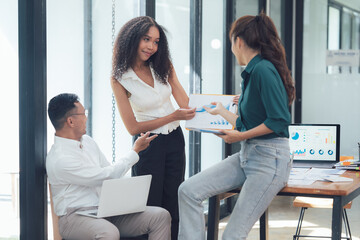 Teamwork Makes the Dream Work: Collaborative Business Meeting. Three diverse professionals engage in a productive discussion, reviewing charts and graphs during a meeting in a modern office setting.